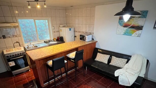 A compact kitchen with a central island, a dining area with a sofa, and a tiled floor. - departamentos egaña (Puerto Montt)