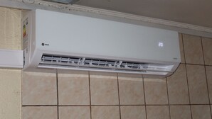 A white air conditioning unit mounted on a tiled wall. - departamentos egaña (Puerto Montt)