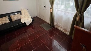 A room with a sofa, a chair, a painting on the wall, a door, and a window with curtains. - departamentos egaña (Puerto Montt)