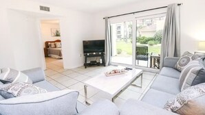 Een moderne woonkamer met een grijze zithoek, een flatscreen televisie en een eettafel.