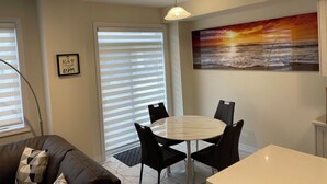 Spiseområde med et rundt bord og stole, en loftlampe, et maleri af en strand ved solnedgang og et indrammet motiverende citat på væggen.