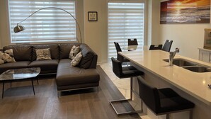 En moderne stue med sofa, sofabord og spiseplads med bar.