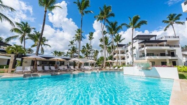 A swimming pool with lounge chairs and umbrellas, surrounded by palm trees and a multi-story building. - Aligio - A Quiet Retreat in Paradise - 2 BR, 2 pools, WiFi, AC, Private Hot Tub (Las Terrenas)