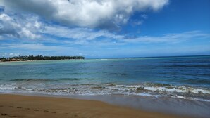 A beach with clear turquoise waters, a sandy shore, and a distant tree-lined shoreline under a partly cloudy sky. - Aligio - A Quiet Retreat in Paradise - 2 BR, 2 pools, WiFi, AC, Private Hot Tub (Las Terrenas)