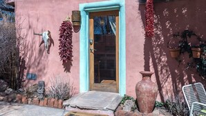 A pink building with a wooden door, a stone wall, and a hanging dried plant.