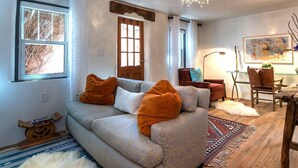 A cozy living room with a sofa, a chandelier, a wooden door, and a rug.