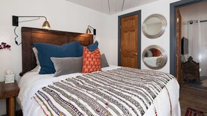 A bedroom with a large bed, two wall-mounted lamps, a wooden headboard, a wooden door, and two round mirrors on the wall.