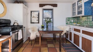 A compact kitchen with a stove, a dining table, and chairs. There is a window with a view of trees outside.