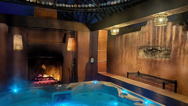 A hot tub with a fire feature, a bench, and decorative lighting.