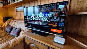 A room with a leather sofa, a TV displaying a Netflix interface, and a wooden wall with a sign above it. - Chalet ideal for relaxing, with breathtaking lake and mountain views (Châtillon)