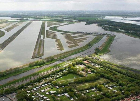 An aerial view of a river with a series of parallel water channels and a residential area with houses and greenery.