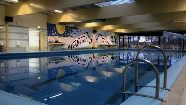 Piscina con un muro revestido de azulejos con un diseño pixelado, una escalera metálica y el reflejo del entorno.