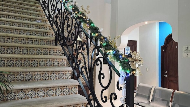 A staircase with ornate black railings and patterned tiles, leading to a landing area with a bench.