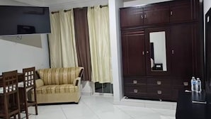 A living room with a sofa, a TV mounted on the wall, a cabinet, and a tiled floor.