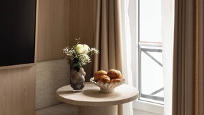 A modern hotel room with a wooden panel wall, a round table with a vase of flowers and croissants, and a large window with curtains. - Charming Studio With AC - 2P- Musee du Louvre (Paris)