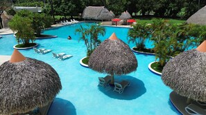 A pool area with thatched umbrellas, lounge chairs, and palm trees.