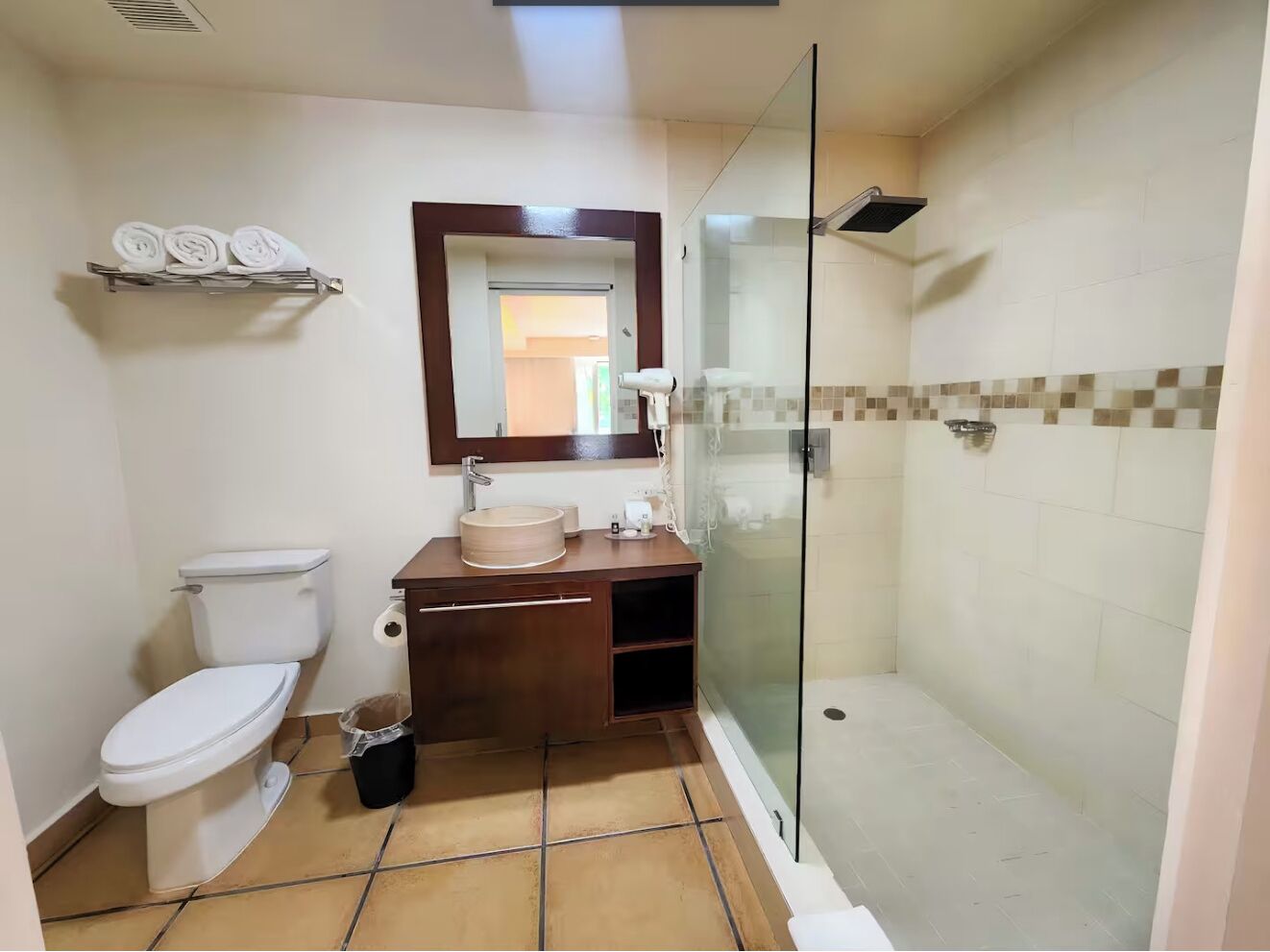 A bathroom with a toilet, sink, mirror, and glass-enclosed shower.