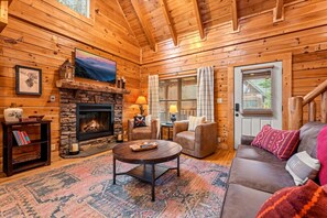 A log cabin interior with a stone fireplace, leather furniture, and a cozy atmosphere. - Luxe Modern Nest: Hot Tub, Swimming Pool, Pets (Pigeon Forge)