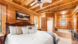 Ein Schlafzimmer einer Holzhütte mit Bett, Fenster, Deckenventilator, Bad mit Badewanne und einer Holztür.