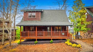 A log cabin with a porch, a small deck, and a stone wall. - Luxe Modern Nest: Hot Tub, Swimming Pool, Pets (Pigeon Forge)