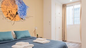Un dormitorio con cama, almohadas, una obra de arte en la pared, una mesita de noche y una ventana.
