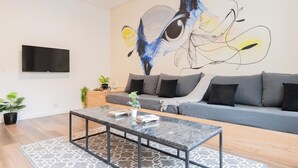 Una sala moderna con un sofá gris, una mesa de centro de cristal y un cuadro abstracto grande en la pared.