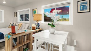 A room with a bed, a white table with a vase of flowers, a lamp, and a window with a view.