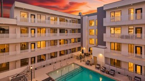 Un hotel de varios pisos con piscina en la azotea, balcones y un cielo al atardecer.