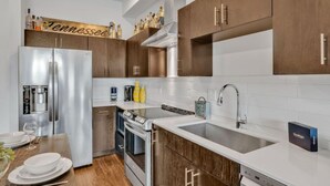 Una cocina moderna con electrodomésticos de acero inoxidable, armarios de madera y encimera blanca.