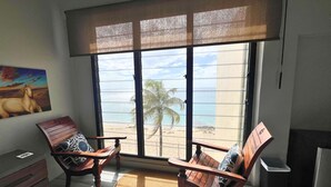A room with a large window overlooking a beach, two wooden chairs, a small table, and a painting on the wall. - Green Flash by the Sea (Frederiksted Southeast)