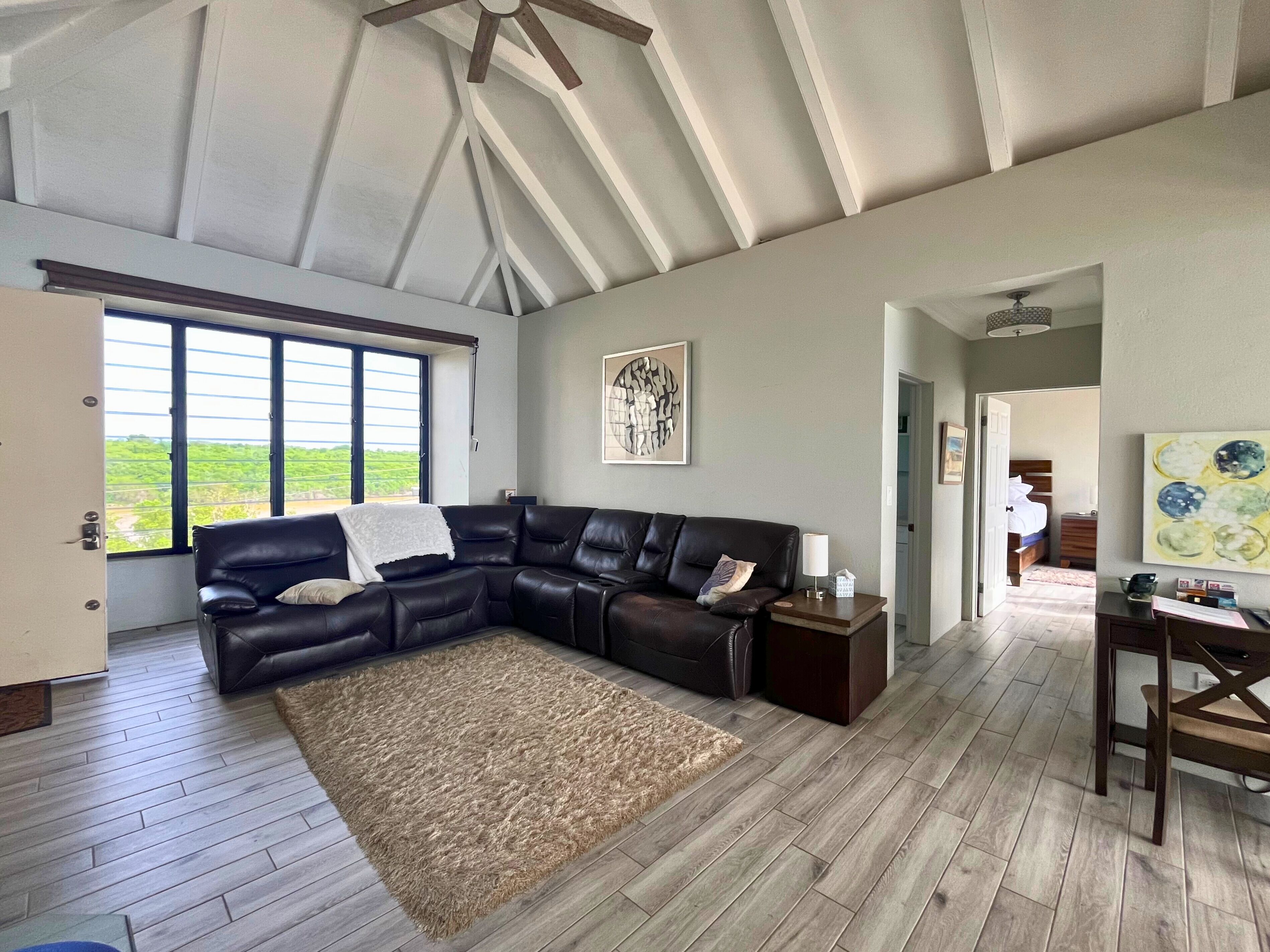 A spacious living room with a large sectional sofa, a wooden floor, and a view through large windows.