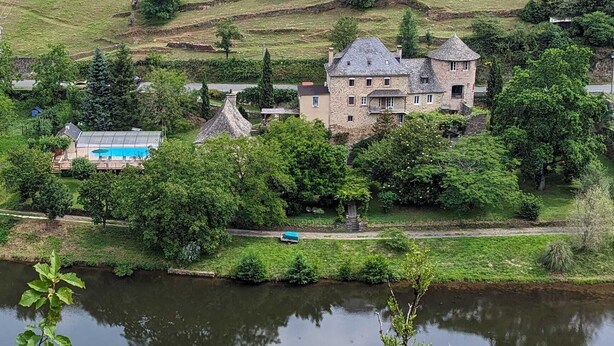 A large stone building with multiple towers, surrounded by lush greenery and terraced fields. - Le Manoir des Pélies-Le clos des Pélies. Gites in an old chapel. (Conques-en-Rouergue)
