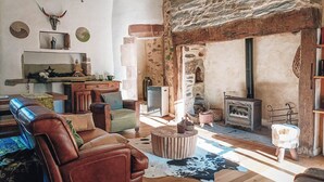 A rustic living room with a stone wall, wooden beams, a fireplace, and a leather sofa. - Le Manoir des Pélies-Le clos des Pélies. Gites in an old chapel. (Conques-en-Rouergue)
