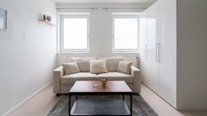 Een moderne, minimalistische woonkamer met een beige bank, twee ramen, een salontafel en een kledingkast.