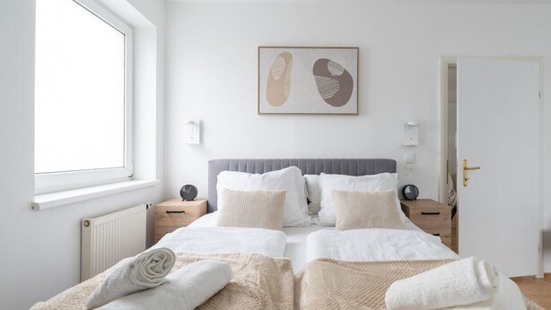 A bedroom with a large bed, two bedside tables, a window, a radiator, and a door. - Spacious Comfort | 55m² | 6 Guests | 24/7 Check-in (Steyr)