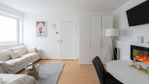 A modern living room with a sofa, a dining table, a fireplace, and a TV mounted on the wall. - Spacious Comfort | 55m² | 6 Guests | 24/7 Check-in (Steyr)