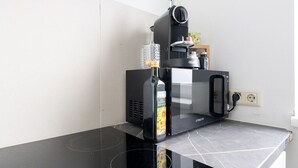 A black espresso machine on a black countertop with a glass bottle of water and a small container of coffee creamer. - Spacious Comfort | 55m² | 6 Guests | 24/7 Check-in (Steyr)
