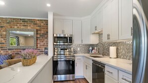 Una cocina moderna con armarios blancos, electrodomésticos de acero inoxidable y una pared decorativa de ladrillo.