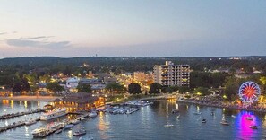 Un paisaje urbano frente al agua, con una noria, barcos amarrados al muelle y edificios al fondo.