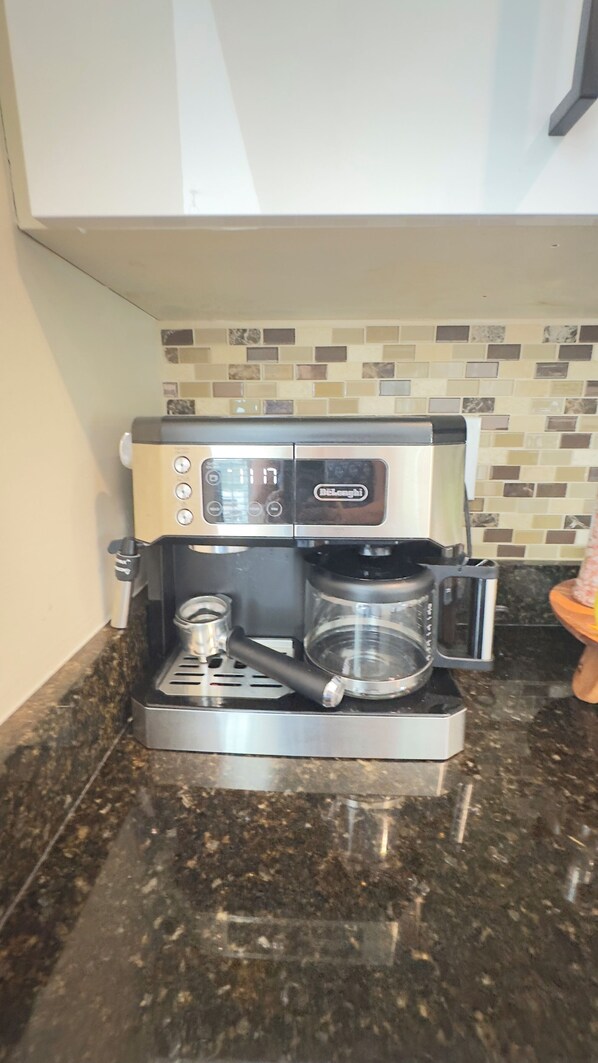 Una cafetera con pantalla digital, jarra de vidrio y portafiltro sobre una encimera de granito.