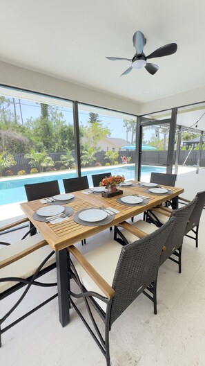 Un comedor con vistas a la piscina, con una mesa de madera, sillas de mimbre y un ventilador de techo.