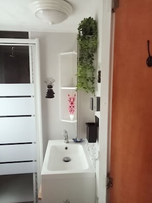 Ein Badezimmer mit weißem Waschbecken, einem Spiegel, einer Topfpflanze und einem Regal mit einer Vase.