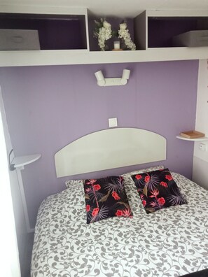 A bed with patterned bedding, a white headboard, and a shelf above with decorative items.