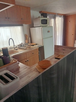 A compact kitchen with wooden cabinets, a microwave, a refrigerator, a sink, and a toaster.