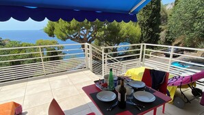 An outdoor patio with a table set for two, surrounded by red chairs, under a blue canopy. - Renovated apartment, sea view, S-W orientation, terrace, near Monaco, Mala beach (Cap-d'Ail)