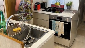 A modern kitchen with a stainless steel sink, a toaster, a stove, and a small oven. There is a shelf above the stove holding various kitchen items. - Renovated apartment, sea view, S-W orientation, terrace, near Monaco, Mala beach (Cap-d'Ail)