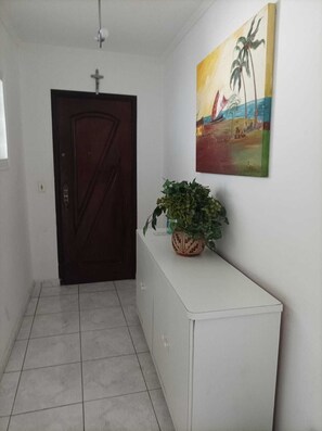 Enter a serene space with a decorative cabinet and a beautiful painting above, leading to a room with a clean and simple aesthetic.