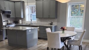 A modern kitchen with grey cabinets, a central island, and a dining area with a round table and chairs. - Newly Remodeled Cottage, 3 Bed, 2 Bath on 5 Acres--Walking distance to 2 Beaches (West Olive)