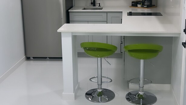 A compact kitchen with white cabinets, a stainless steel refrigerator, a microwave, and a coffee maker. There are two green bar stools under the counter. - Seda Verde (Kissimmee)