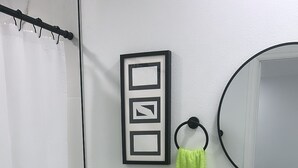 A bathroom with a toilet, sink, mirror, and a framed picture on the wall. - Seda Verde (Kissimmee)